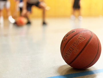 Basketball liegt in einer Turmhalle im Hintergrund Jugendliche